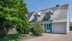 Une maison à deux étages avec une allée gravillonnée, un petit jardin et une clôture en bois.