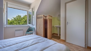 Une chambre avec un grand lit, une fenêtre, une chaise, une salle de bain avec un lavabo et une porte.