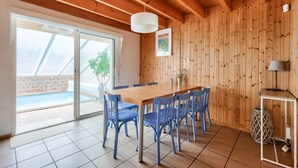 A dining area with a wooden table and blue chairs, a white pendant light, and a view of an outdoor swimming pool through large glass doors. - 600 m from the sea, house for 8 adults / 2 children (La Faute-sur-Mer)