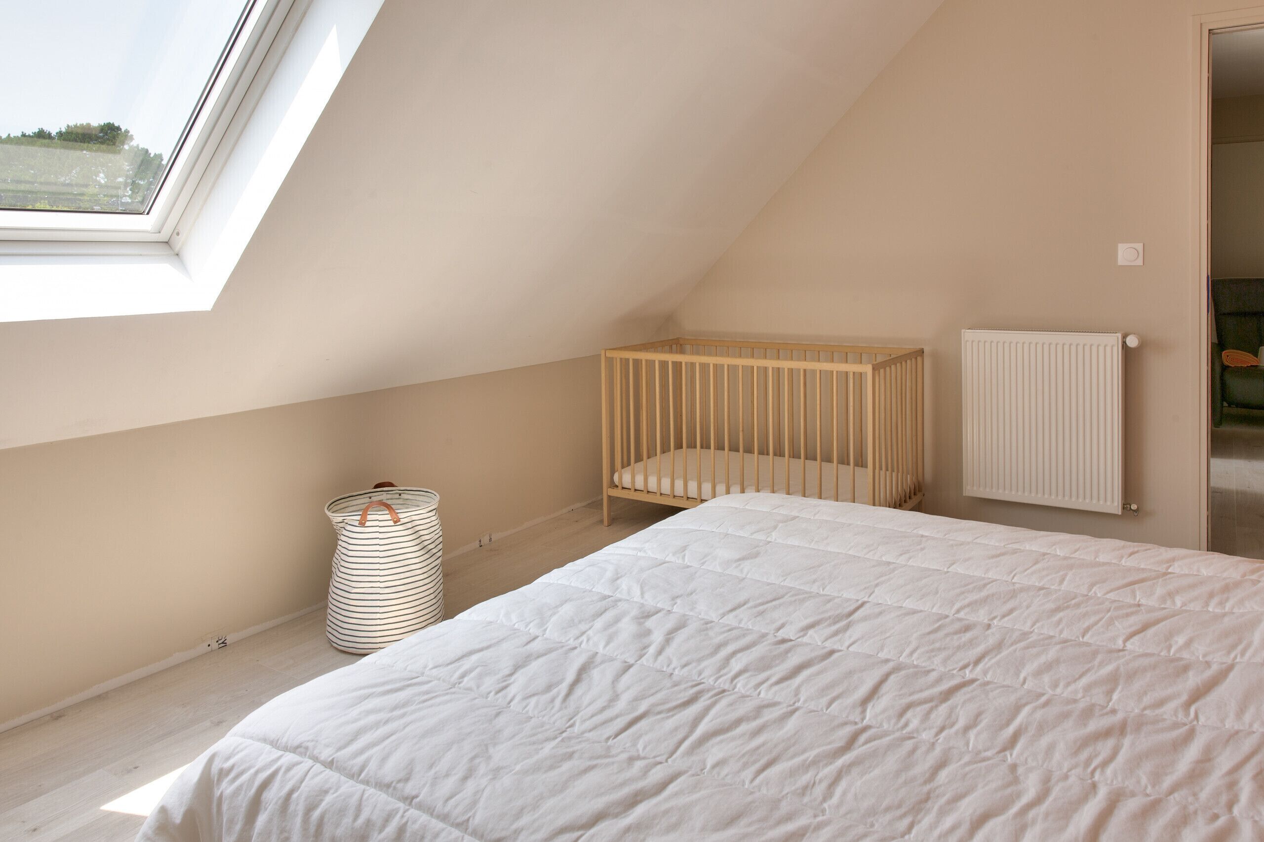 Une chambre avec un plafond en pente, un berceau, un radiateur et une fenêtre.