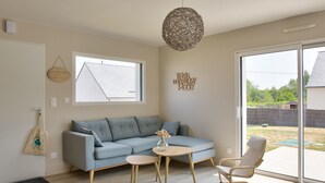 A modern living room with a light blue sofa, a round wooden coffee table, a white armchair, and a large window offering a view of the backyard. - House for 8 with garden 1km from the beach (Plobannalec-Lesconil)