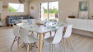 A modern dining area with a round table, white chairs, and a glass-top table. - House for 8 with garden 1km from the beach (Plobannalec-Lesconil)