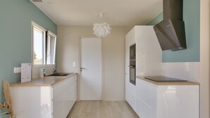 A modern kitchen with white cabinetry, a built-in oven, and a window with blinds. - House for 8 with garden 1km from the beach (Plobannalec-Lesconil)
