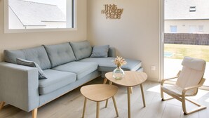 A modern living room with a light blue sectional sofa, a round wooden coffee table, a white armchair, and a decorative wall piece. - House for 8 with garden 1km from the beach (Plobannalec-Lesconil)