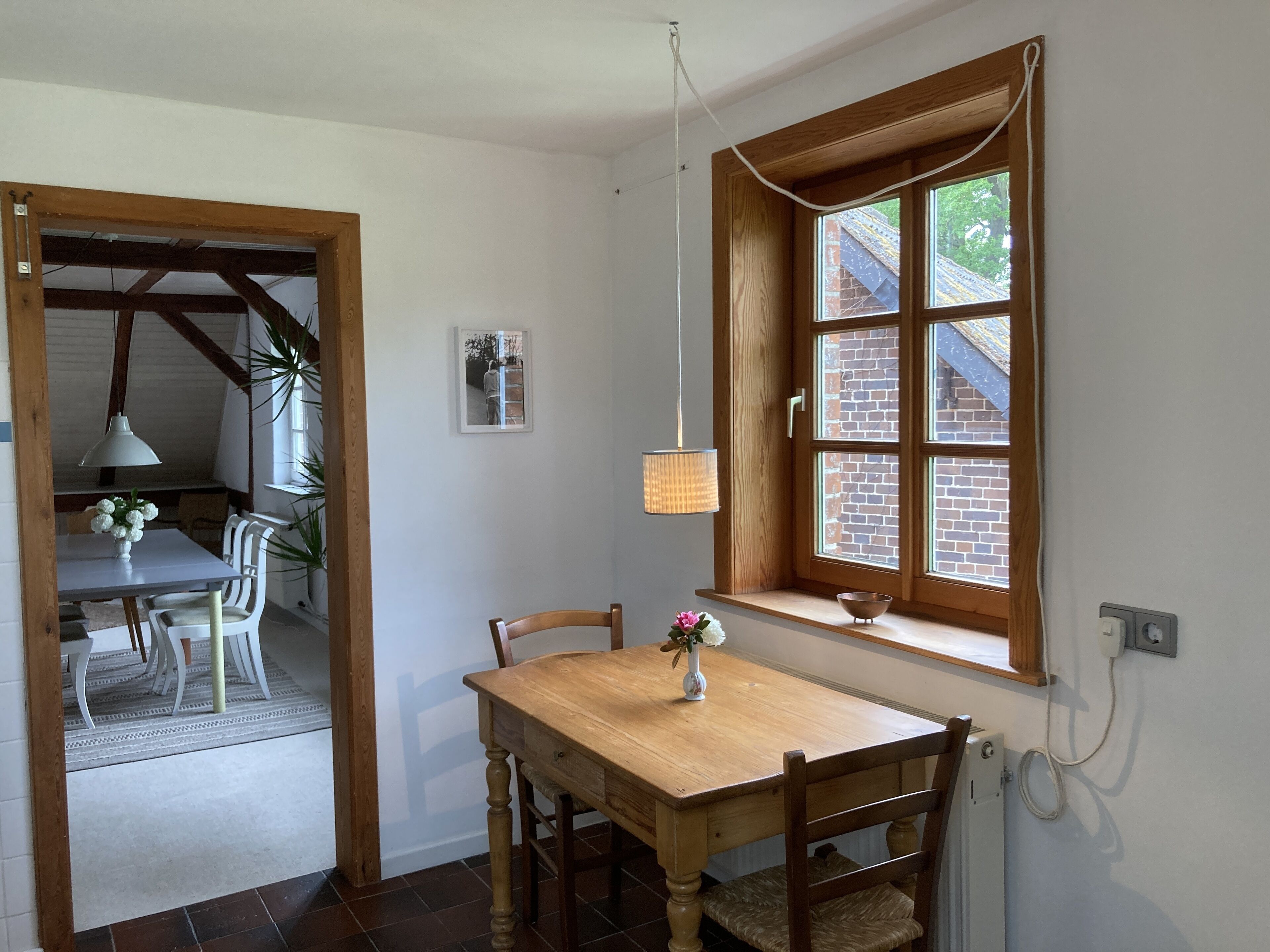 Un coin repas avec une table et des chaises en bois, une fenêtre donnant sur un bâtiment en briques et un luminaire suspendu.