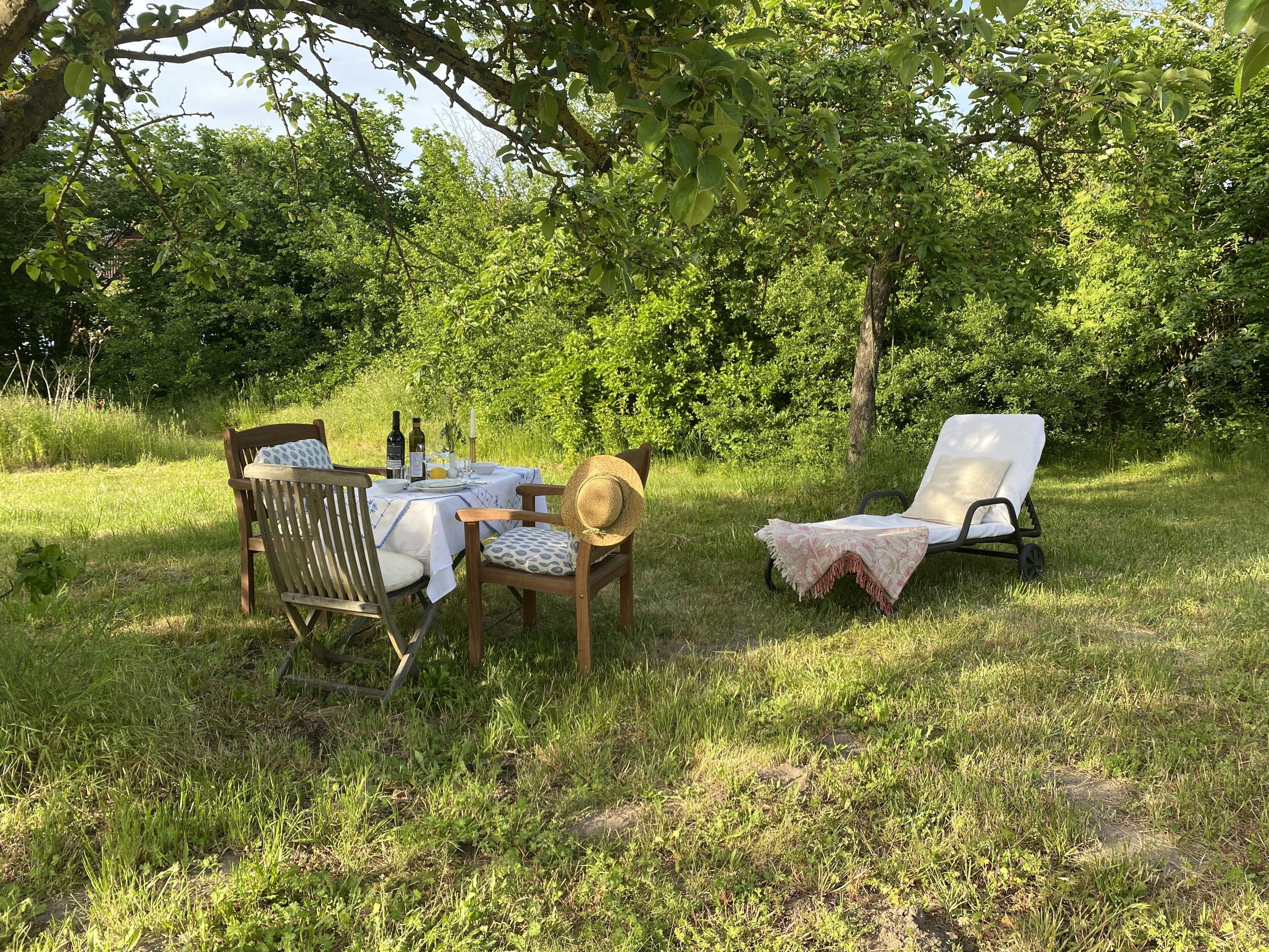 An outdoor dining area with a table set for two, surrounded by lush greenery and trees.