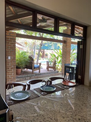 Un espace repas avec vue sur le jardin, des sièges d’extérieur et un ventilateur de plafond.