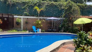 Una piscina con borde de ladrillo, rodeada de plantas en macetas y mobiliario de exterior.