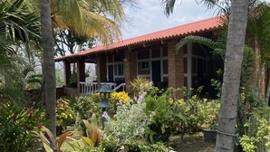 Una casa con techo rojo y paredes de ladrillo, rodeada por un jardín con diversas plantas y una jardinera grande al frente.