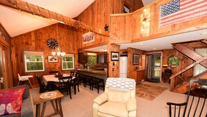 A wooden interior with a dining area, a cream-colored armchair, and a staircase.