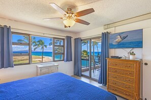 Een slaapkamer met een bed, een plafondventilator, een dressoir en uitzicht op het strand door grote ramen.