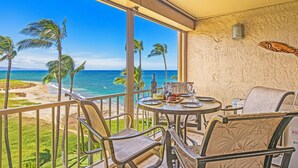 Een balkon met uitzicht op de oceaan, palmbomen en een tafel gedekt met een fles, glazen en een bord eten.