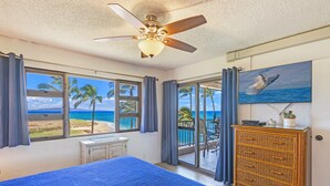 Een slaapkamer met een bed, een plafondventilator, een dressoir en uitzicht op het strand door grote ramen.