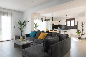 A modern living room with a sectional sofa, a coffee table, and a dining area. - Waves of Blue Villa with Sea View (Tsairi)