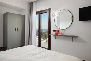 A bedroom with a bed, a wardrobe, a sliding glass door to a balcony, a round mirror, and a mounted TV. - Waves of Blue Villa with Sea View (Tsairi)