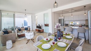 A modern living room with a sofa, coffee table, and a dining area set with a table, chairs, and a vase of flowers.