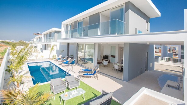 A modern two-story house with a swimming pool, outdoor seating, and a view of the surrounding landscape.