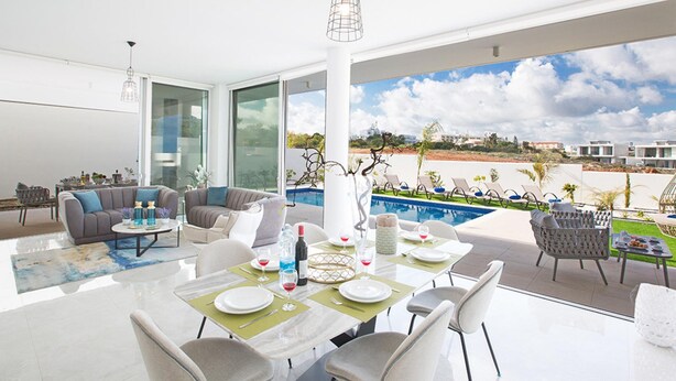 Un comedor moderno con una mesa dispuesta para cuatro personas, con vistas a una piscina y un jardín ajardinado.