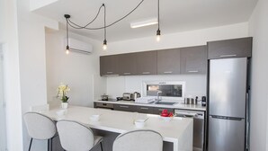Cocina moderna con una isla central, taburetes de bar, electrodomésticos de acero inoxidable e iluminación colgante.