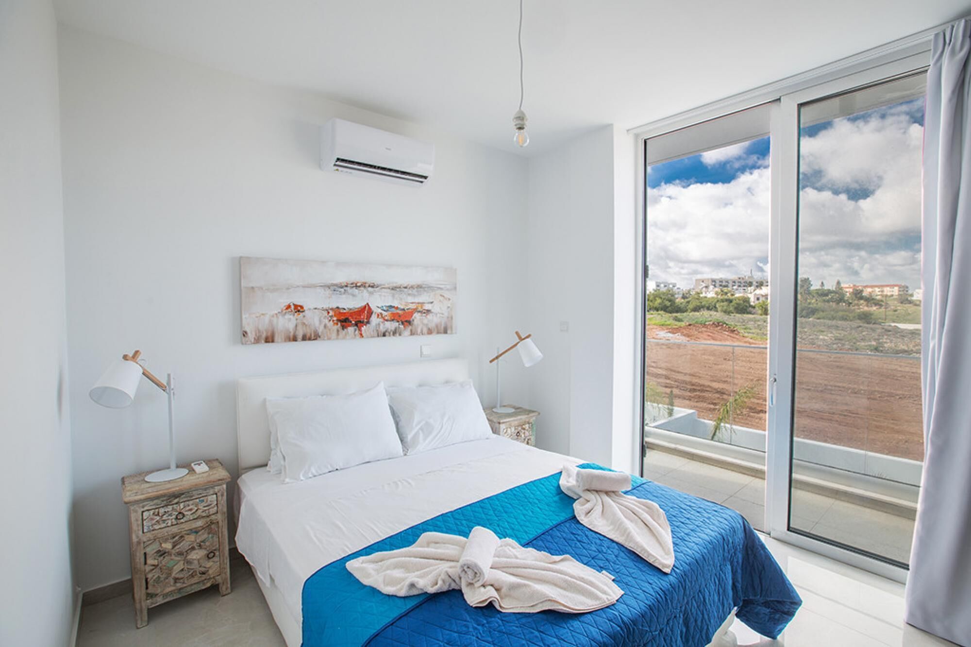 Een slaapkamer met een bed, een schilderij, een airconditioner, bedlampen en uitzicht op het landschap.