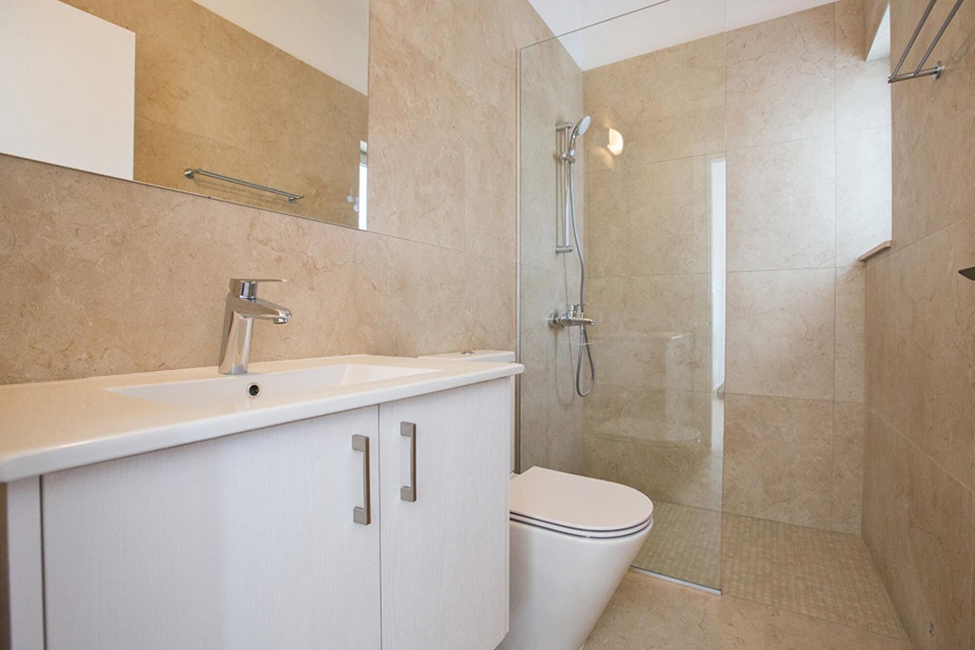A modern bathroom with a white sink, a mirror, a toilet, and a glass-enclosed shower area.
