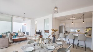 Un espace de vie moderne à aire ouverte, comprenant une table à manger pour quatre personnes, une cuisine avec des tabourets de bar et une grande fenêtre qui laisse entrer la lumière naturelle.