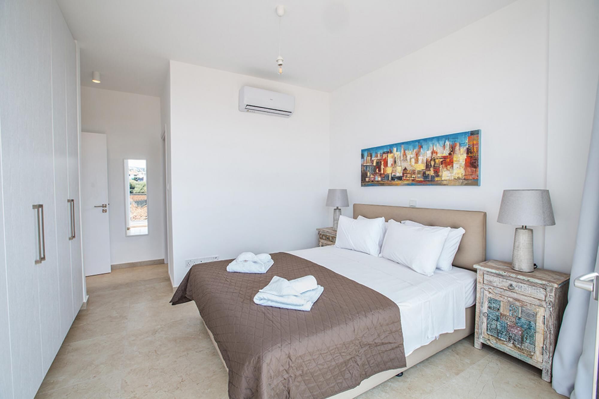 Quarto de hotel com uma cama grande, um quadro na parede, um aparelho de ar condicionado e vista pela janela.