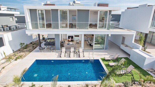Une maison moderne à deux étages dotée d’une grande piscine, d’un espace extérieur aménagé pour se détendre et d’un jardin bien entretenu.