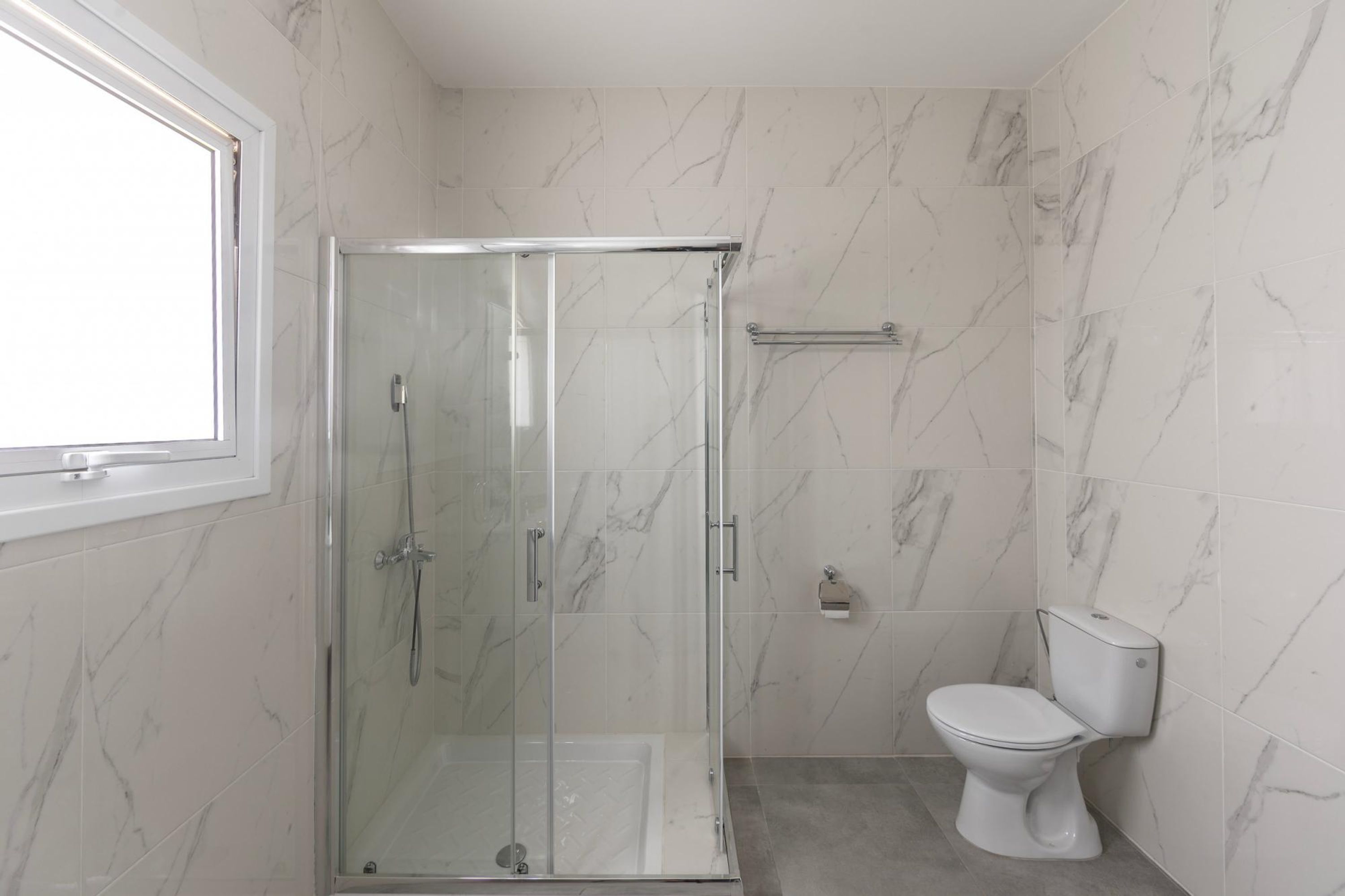 Baño con cabina de ducha de vidrio, inodoro y paredes con diseño de mármol.