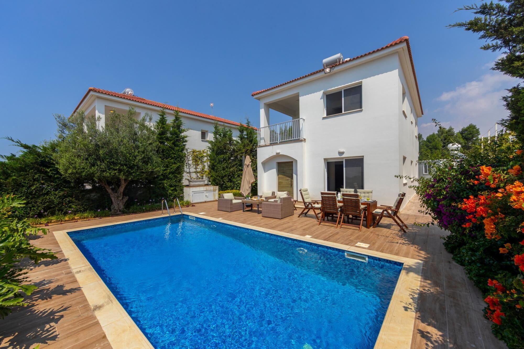 Una casa de dos pisos con piscina, muebles de exterior y jardín.