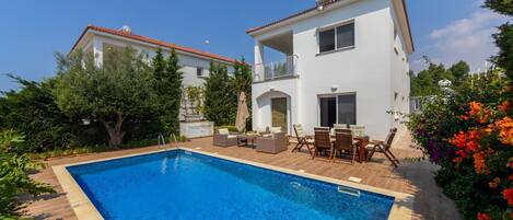 Una casa de dos pisos con piscina, muebles de exterior y jardín.