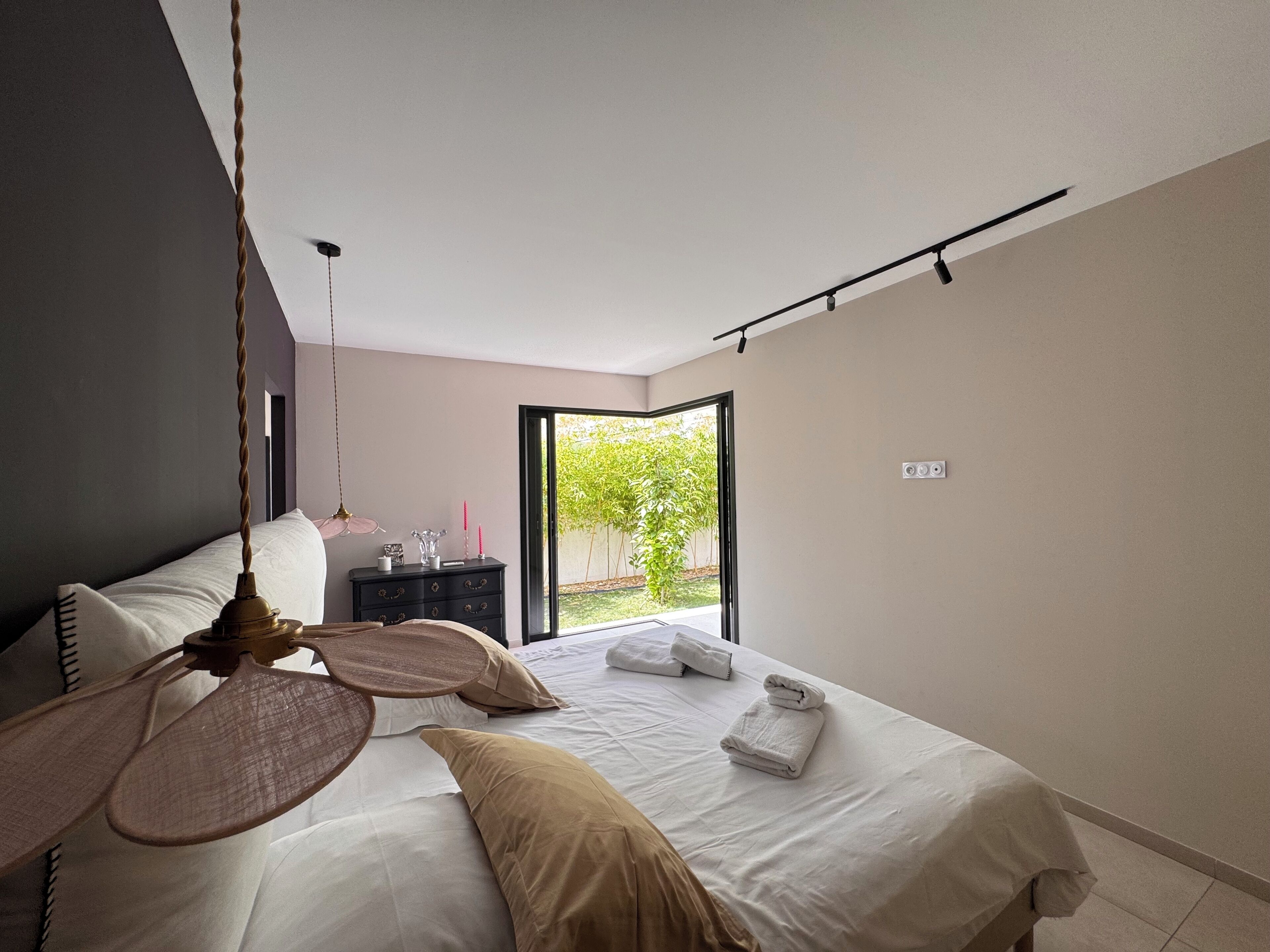 Een moderne slaapkamer met een bed, nachtkastje en uitzicht op een tuin door een schuifdeur.