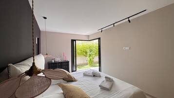 Een moderne slaapkamer met een bed, nachtkastje en uitzicht op een tuin door een schuifdeur.