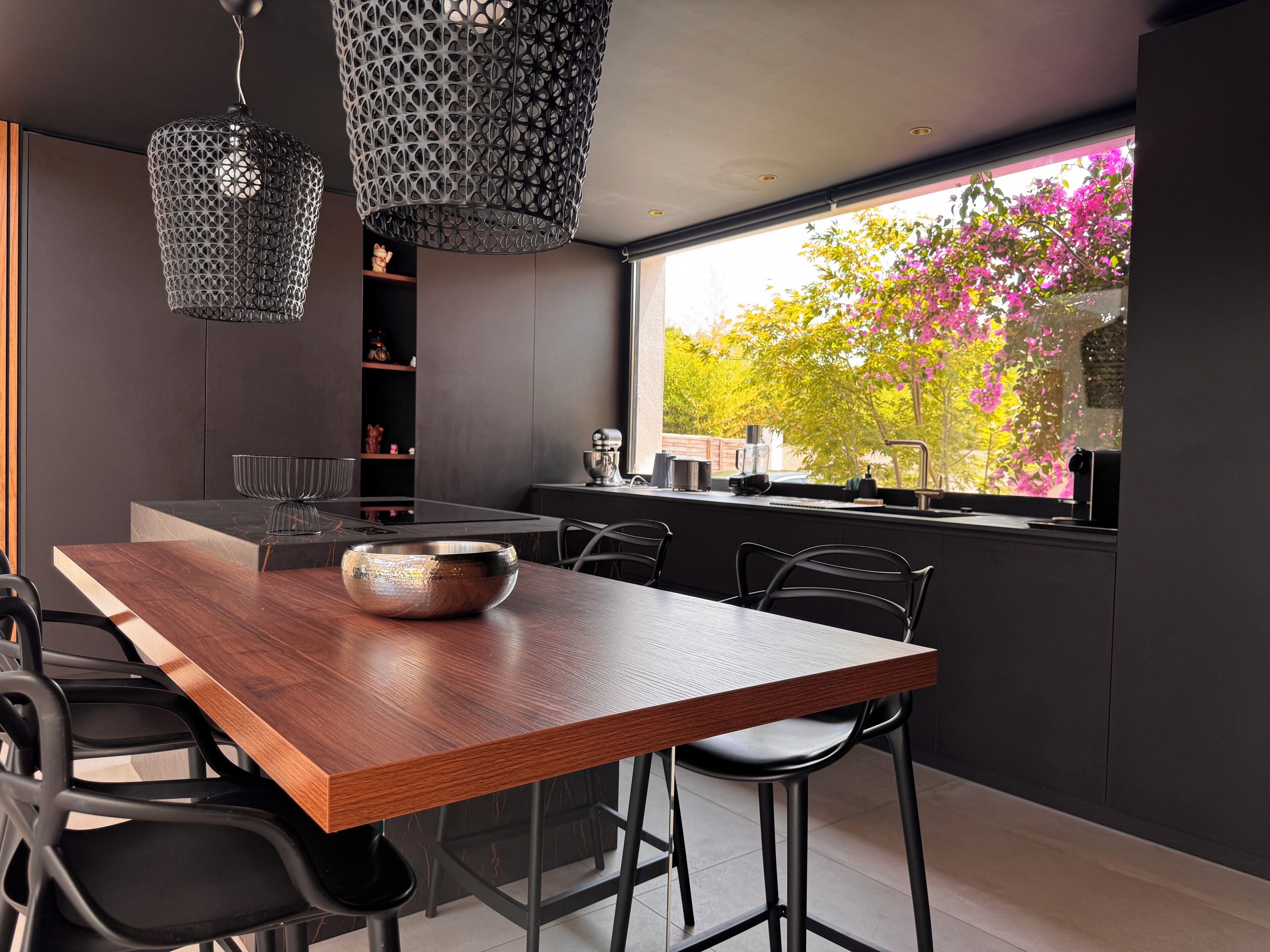 Een moderne keuken met een houten eettafel, zwarte stoelen en hanglampen.