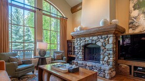 A cozy living room with a stone fireplace, large windows, a comfortable sofa, and a television.