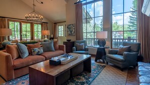 A spacious living room with a large window, a wooden coffee table, a sofa, and a chair.
