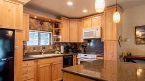 A kitchen with wooden cabinets, granite countertops, a refrigerator, a microwave, a stove, and a sink. - Alpine Villa Condo 1- Find a Perch in Ketchum at Treehouse Condo (Ketchum)