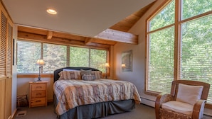 A bedroom with a large bed, a chair, a nightstand, and a window with blinds. - Alpine Villa Condo 1- Find a Perch in Ketchum at Treehouse Condo (Ketchum)