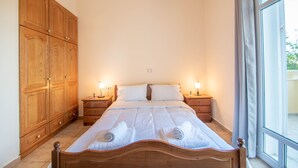 A bedroom with a wooden bed, two bedside tables with lamps, a large wardrobe, and a window with curtains. - Andelica Holiday Villa (Zakynthos)