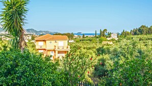 A two-story building with a tiled roof, surrounded by lush greenery and a clear blue sky. - Andelica Holiday Villa (Zakynthos)