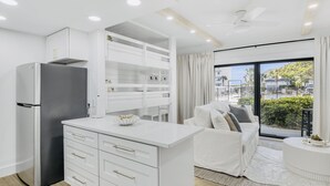 A modern kitchen with white cabinetry, a built-in oven, and a refrigerator. There is a dining area with a white table and chairs, and a large window offering a view of the outside. - Private Beach|Bikes|Pool|Next2Seaside (Santa Rosa Beach)