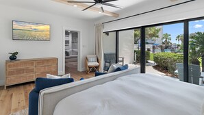 A modern hotel room with a large bed, a ceiling fan, a rattan side table, and a view of the pool and palm trees outside. - Private Beach|Bikes|Pool|Next2Seaside (Santa Rosa Beach)