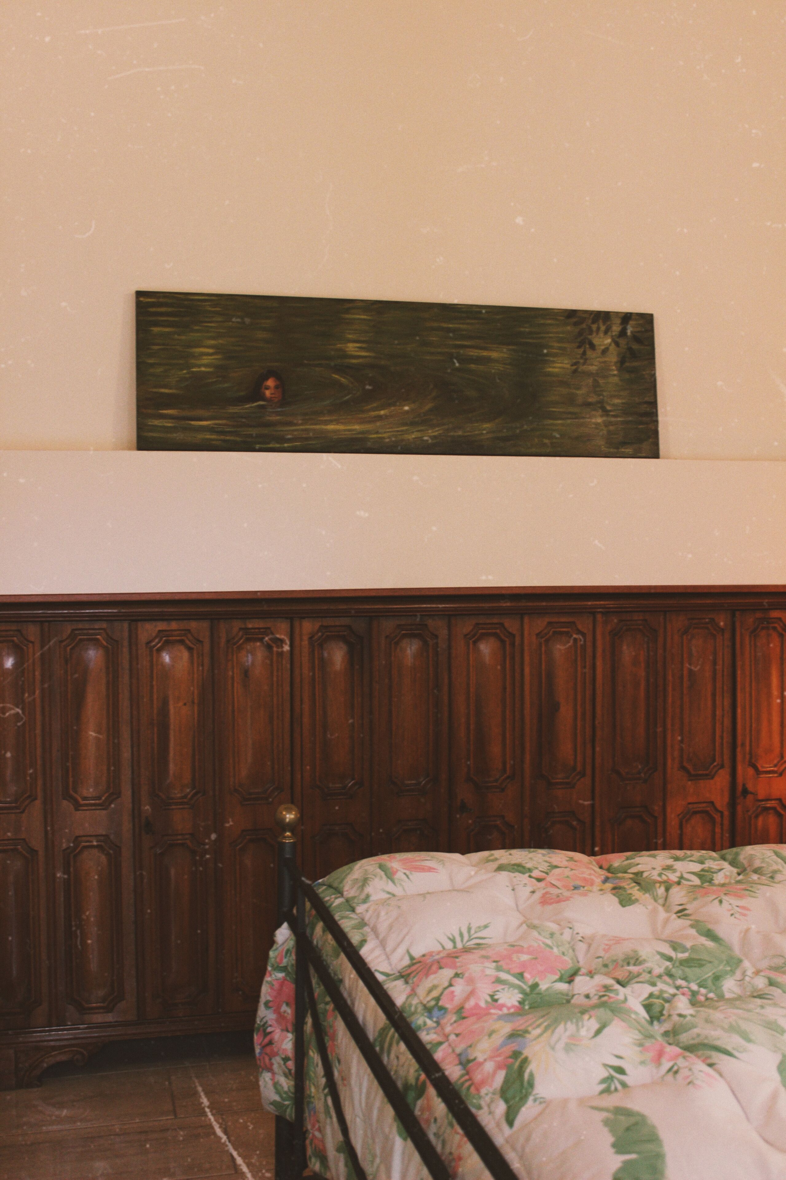 Um quarto com cabeceira de madeira, colcha florida e um quadro na parede.