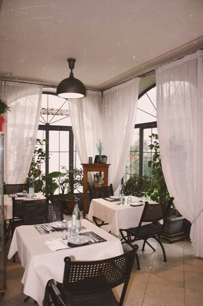 A dining area with tables set for two, featuring white tablecloths, black chairs, and a hanging light fixture. - Villa Franca (Passirano)