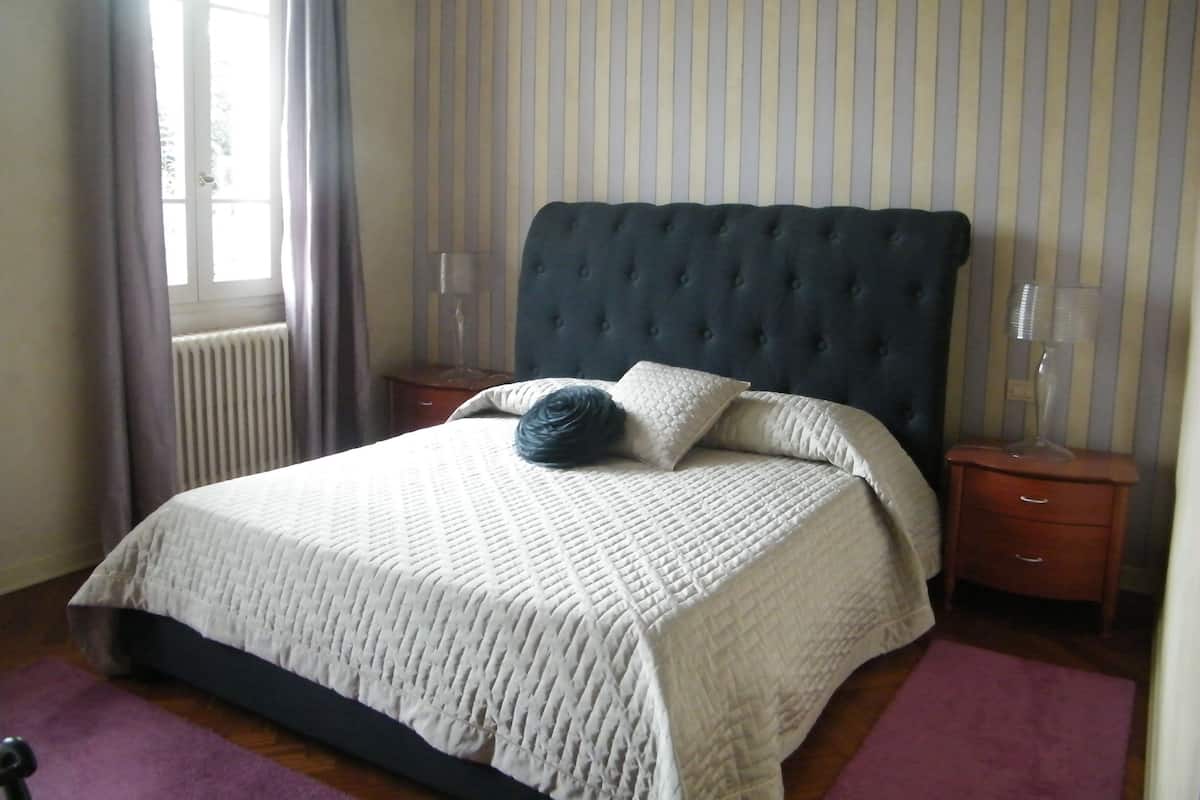 A neatly made bed with a quilted white duvet, a dark headboard, and two bedside lamps on wooden nightstands.