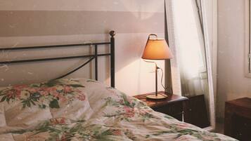Una cama con ropa de cama floral, una lámpara de noche, un espejo y una pared con rayas horizontales.
