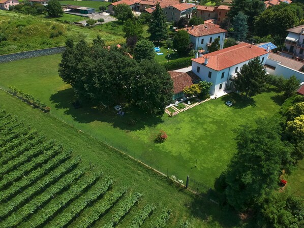 An aerial view of a residential area with a large house, a well-maintained lawn, and a vineyard. - Villa Franca (Passirano)