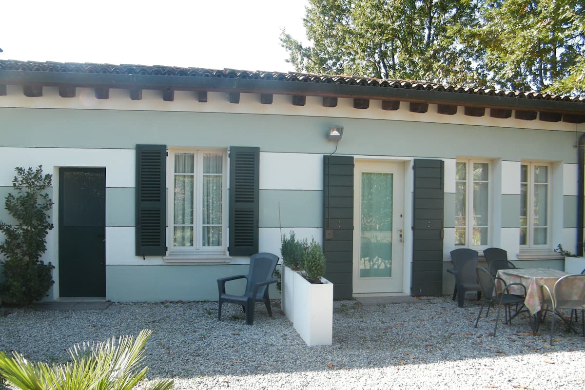 A building with a tiled roof, a gravel driveway, and a patio area with chairs and a table.