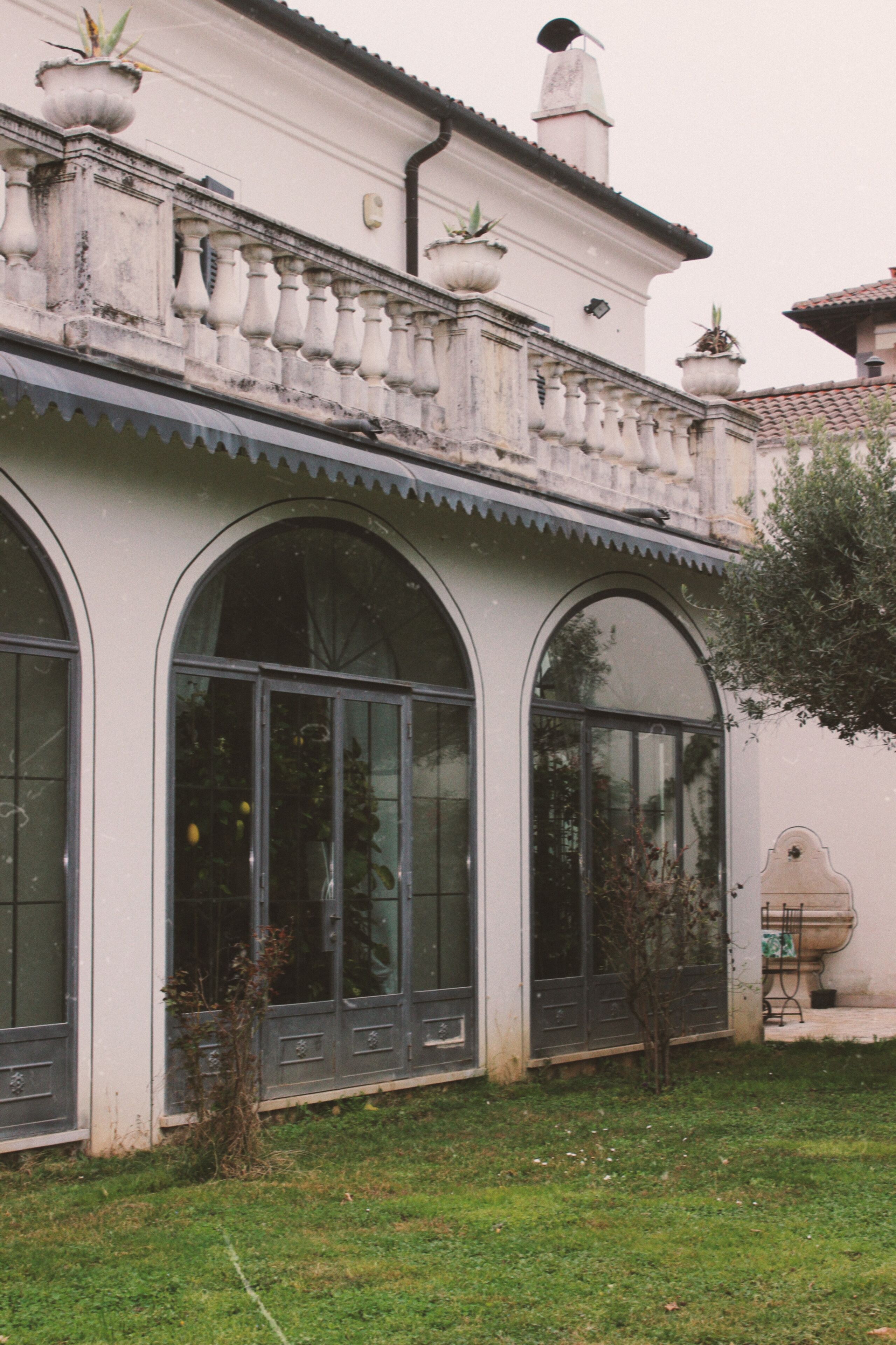 A building with large arched windows, a balcony with potted plants, and a small garden area.