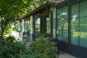Un patio exterior cubierto con paredes de cristal, plantas en macetas y mobiliario de exterior.